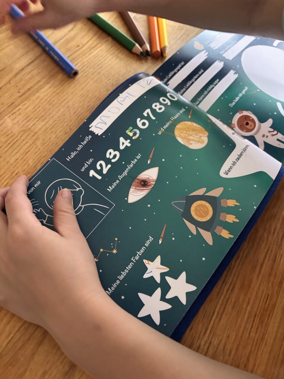 Eine Hand hält ein Buch mit bunten Illustrationen von Zahlen, Sternen und einem Auge.