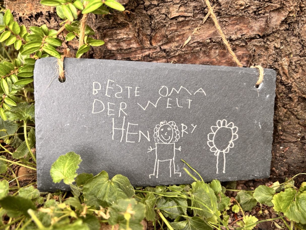 Kreidetafel mit der Aufschrift "Beste Oma der Welt" und einfachen Zeichnungen von Figuren.