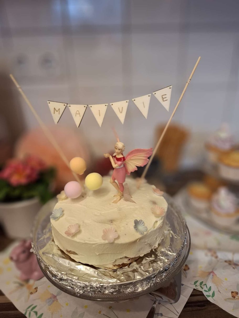 Torte mit Zuckerdekor, einem Engel und bunten Kügelchen, dekoriert mit Fähnchen.