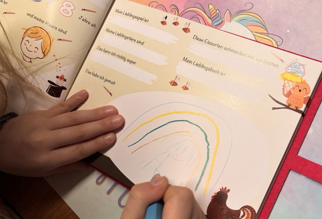 Kind schreibt mit einem gelben Stift in ein Freundebuch mit dem Thema Weltraum