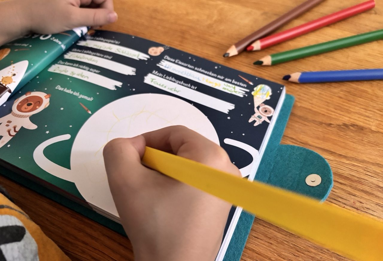 Kind schreibt mit einem gelben Stift in ein Freundebuch mit dem Thema Weltraum