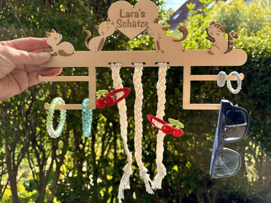 Ein Holzanhänger mit mehreren Haken für Schmuck und Accessoires in einer grünen Umgebung.